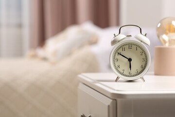 Stylish alarm clock on white nightstand indoors. Space for text