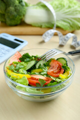 Calculator, tasty salad in bowl and other food on wooden table. Weight loss concept