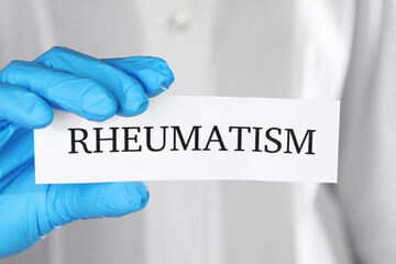 Doctor in glove holding sheet of paper with word Rheumatism, closeup