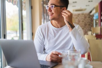 A young businessman in cafe using his laptop mobile phone and wireless earbuds while working on his project business on his laptop and talking on the phone 