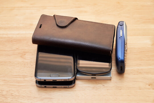 Several Old Used Up Cell Phones From Different Decades Piled Up On The Table