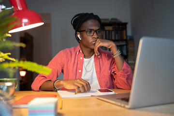 Exhausted bored African male student looking at laptop screen, unhappy black guy wearing wireless...