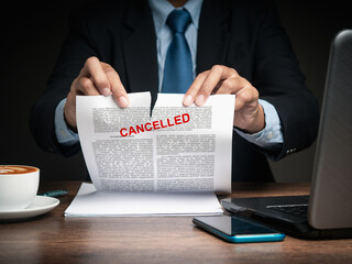 Businessman in a suit tearing up a canceled contract while sitting at the table - obrazy, fototapety, plakaty