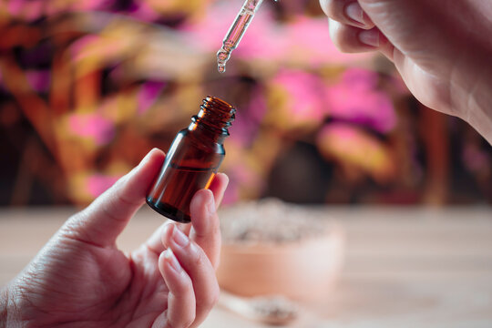 Hands holding a bottle of CBD oil and its dropper lid, with hemp leaf in the background. Legalized CBD product for medical purposes.