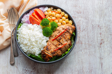 Healthy food grilled chicken has rice and vegetable in bowl on white wood table.
