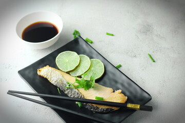 1 piece of salmon served in Japanese style in a black plate at a Japanese restaurant.