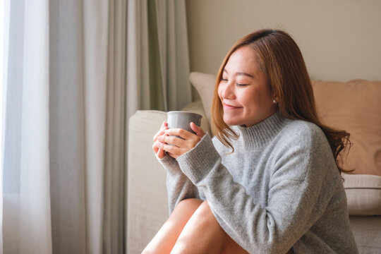 Portrait image of a beautiful young asian woman holding and drinking hot coffee while relaxing at home