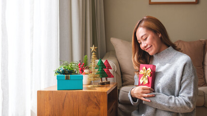 Portrait image of a young woman in sweater holding present box with Christmas holiday decoration at home