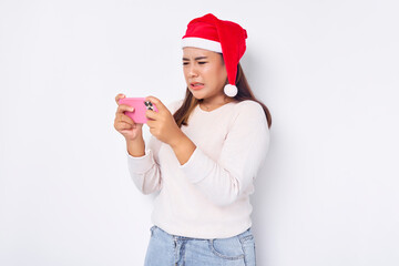 Angry young Asian woman in a Christmas hat playing game with smartphone isolated over white background. celebration Christmas holiday and New Year concept