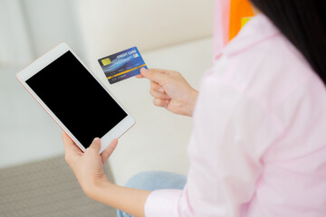 Young asian woman holding credit card shopping online with tablet computer blank display screen buying and payment, female using debit card purchase or transaction, business and ecommerce concept.
