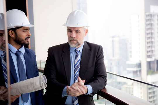 Senior architect inspector talking with contractor man together at office while holding blueprint building structure, executive and engineer planning project, industry and construction concept.