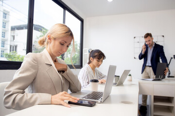 Young caucasian businesswoman using laptop computer and smart phone working at the office, woman and colleagues working with confident at workplace, startup business concept.