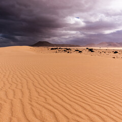 Fototapeta na wymiar Structured sand dunes with dark volcano and highway against stormy and cloudy sky, Corralejo, Spain