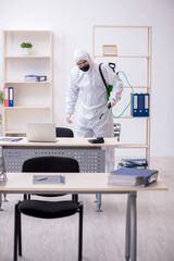 Young male contractor disinfecting office during pandemic