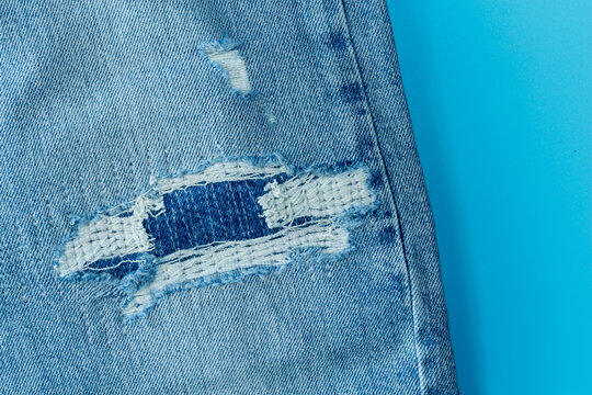 Hole On Denim Jeans. Ripped Destroyed Torn Blue Jeans Background. Close Up Blue Denim Jean Texture .