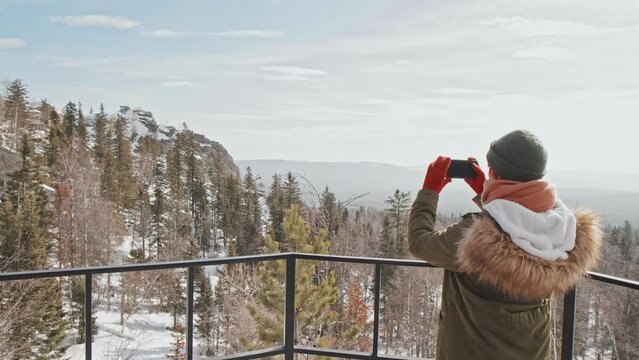 Unrecognizable young woman spending weekend hiking in mountains walking to observation deck taking photos of scenery on smartphone