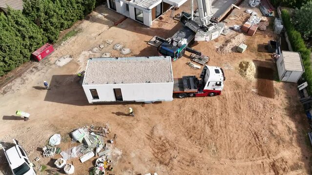 Pre-fabricated modular house trasported by truck to construction site. Aerial top-down circling