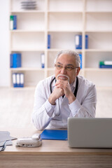 Naklejka premium Old male doctor working in the clinic