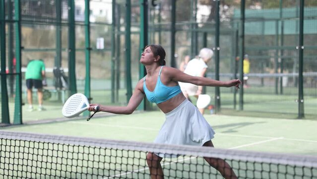 Female player playing padel in a padel court outdoor behind the net
