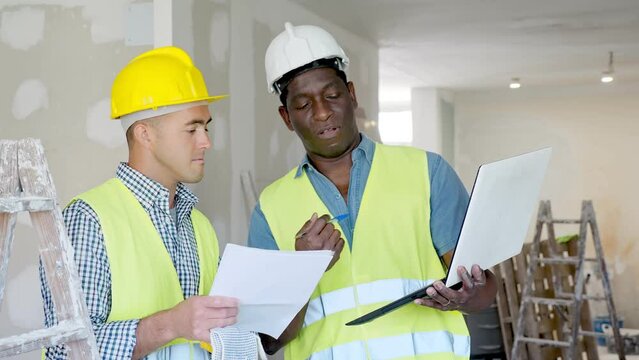 African-american and caucasian men engineers discussing work plan, using laptop in apartment. 