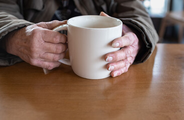 Old woman holding cup of hot coffee drink in her hands. Closeup of an elderly womans hand holding a cup of tea or coffee