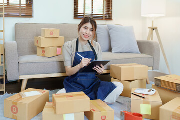Starting small business entrepreneur of independent young Asian woman online seller is using smart phone and taking orders to pack products for delivery to customers. SME delivery concept