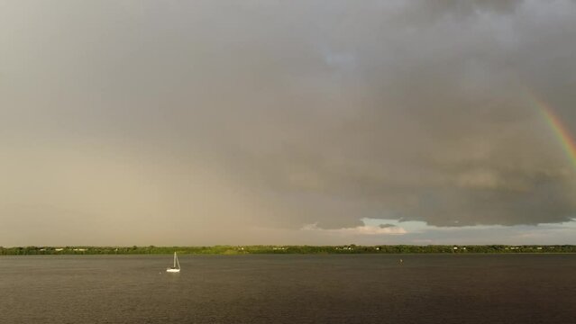 Video of a lake after the storm with sailboat, dark clouds and panning from right to left showing both side of the rainbow