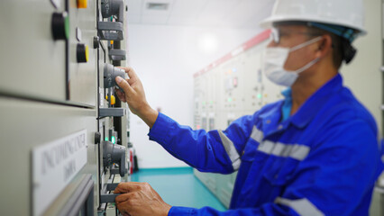 An electrical maintenance worker working in a station building inspects an electrical control panel to maintain the stability of the voltage supply to industrial plant. Energy industrial concept