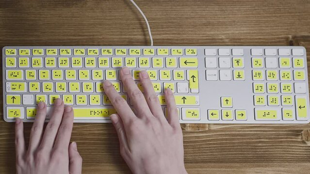 Close-up of a computer keyboard with braille. A blind girl is typing words on the buttons with her hands. Technological device for visually impaired people. Tactilely touches bumps on the keys