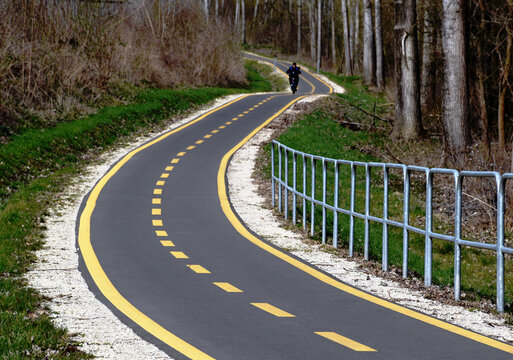 winding asphalt bicycle path. spring nature scene. dense forest on the side. yellow painted dashed divider. two lanes. diminishing perspective. exercise and outdoor activities.