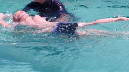Swimming coach teaches a kid to swim. Caucasian child learning to swim in the pool in summer wearing swimming goggles. Slow motion.