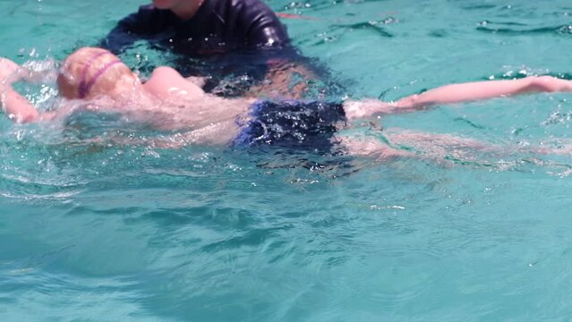Swimming coach teaches a kid to swim. Caucasian child learning to swim in the pool in summer wearing swimming goggles. Slow motion.