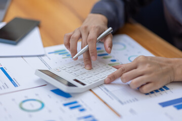 Asian Businesswoman Using laptop computer and working at office with calculator document on desk, doing planning analyzing the financial report, business plan investment, finance analysis concept.
