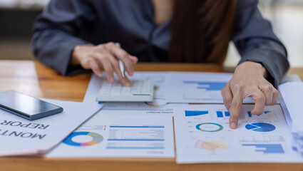 Asian Businesswoman Using laptop computer and working at office with calculator document on desk, doing planning analyzing the financial report, business plan investment, finance analysis concept.
