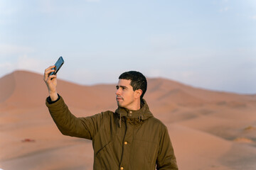 young man takes a selfie with his smartphone in the middle of the desert