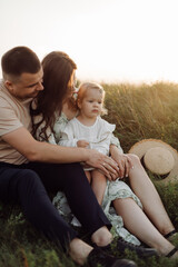 Fototapeta premium Beautiful caucasian family of father, mother and little daughter posing on camera on background of green field