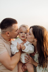 Beautiful caucasian family of father, mother and little daughter posing on camera on background of green field