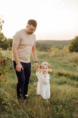 Fototapeta premium Beautiful caucasian family of father, mother and little daughter posing on camera on background of green field