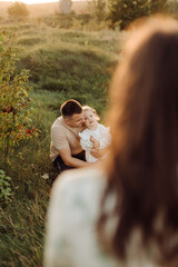 Beautiful caucasian family of father, mother and little daughter posing on camera on background of green field