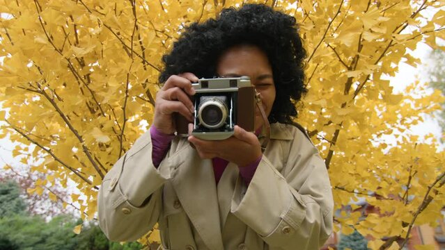 Close-up shot professional female photographer snapping autumn nature outdoors. Portrait of a woman holding retro-styled camera while strolling in the park. High quality 4k footage