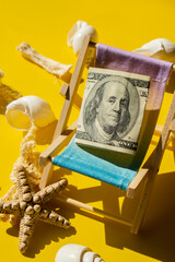 Rolled Up Hundred Dollar Banknote On Miniature Deck beach Chair. Concept of costs in travel...