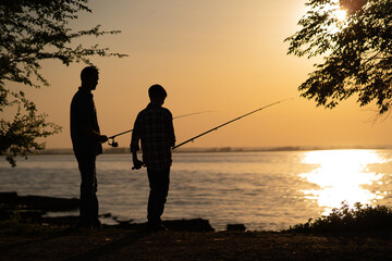 silhouette of man and teen boy fishing on the lake