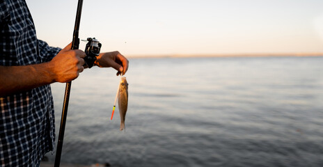 Caught fish hanging on fishing rod, lake in the background, outdoors. hobby, activity, leisure, fishing concept.