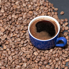A cup of brewed black coffee on a dark background with beans.