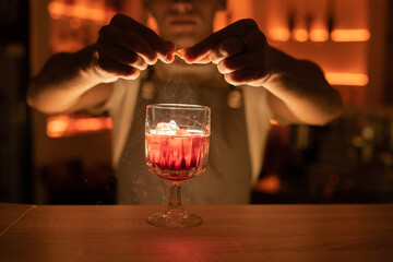 Barman sprinkling the orange juice into the cocktail on bar counter.