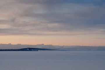 Bridge over a river covered in ice. In the background is the city and the sunset sky.