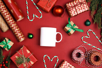 White coffee mug with Christmas gifts and decorations on a red background.