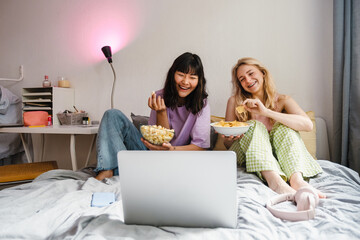 Two multiracial girls eating snacks while watching movie together