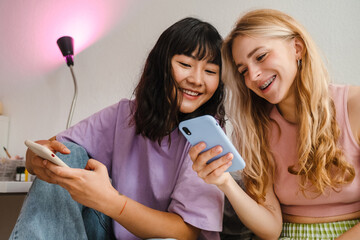 Two multiracial girls laughing while using mobile phones together