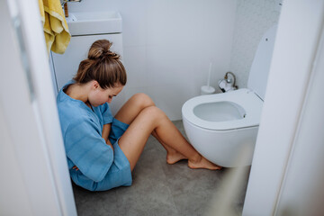 Young sick woman sitting on floor near toilet. - obrazy, fototapety, plakaty
